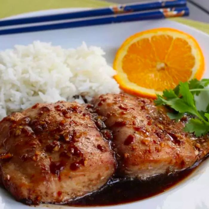 A perfectly seared fish fillet glazed with ginger-soy, served alongside fluffy white rice, an orange wedge, and a touch of parsley garnish.