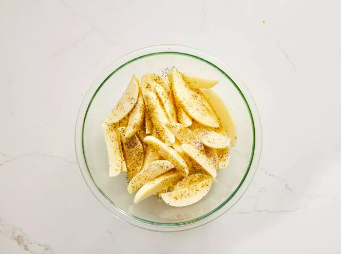 raw potato wedges in a mixing bowl, seasoned with salt and black pepper.