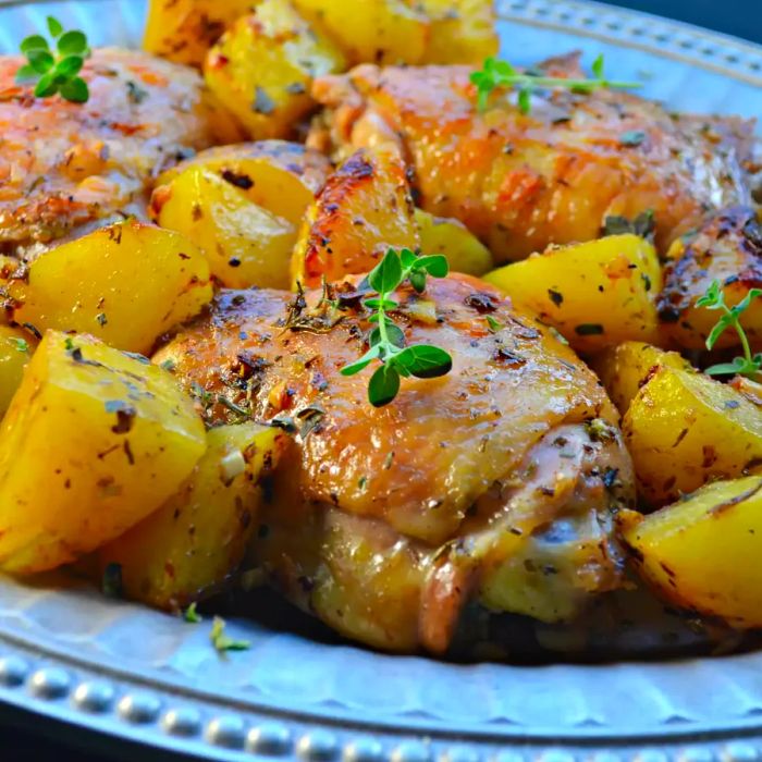 A platter of crispy chicken thighs served with roasted potatoes, topped with fresh thyme