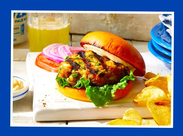 A perfectly grilled turkey burger served on a bun, with sides and a refreshing beer in the background.