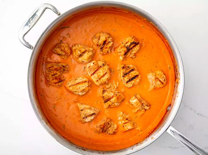 An overhead view of grilled chicken cooking in a rich Tikka Masala sauce.