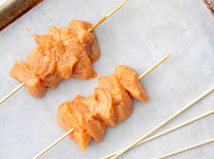 An overhead view of two raw chicken skewers resting on a baking sheet.