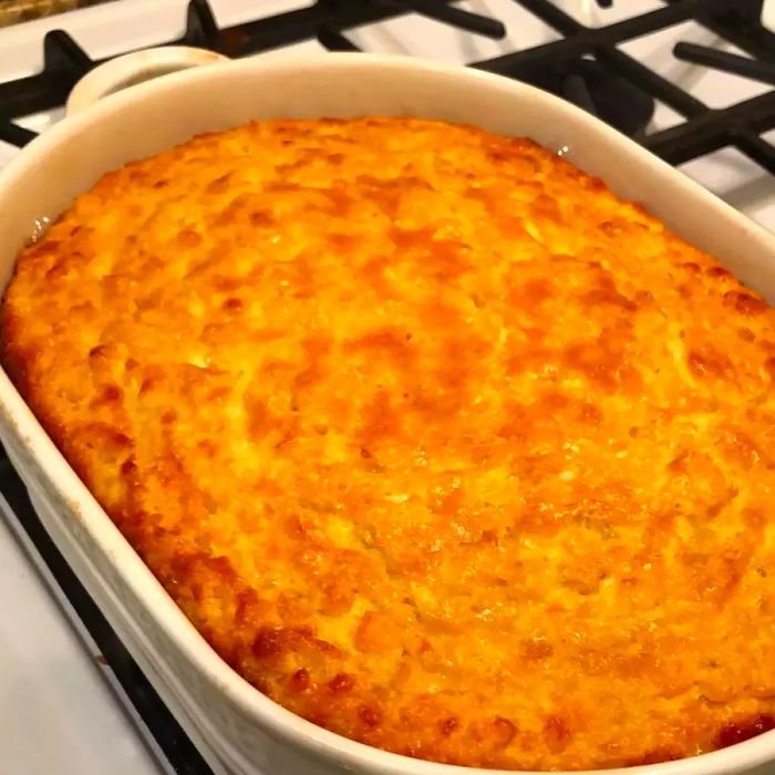 A white ceramic casserole dish filled with golden-brown baked corn pudding, its edges crisped to perfection