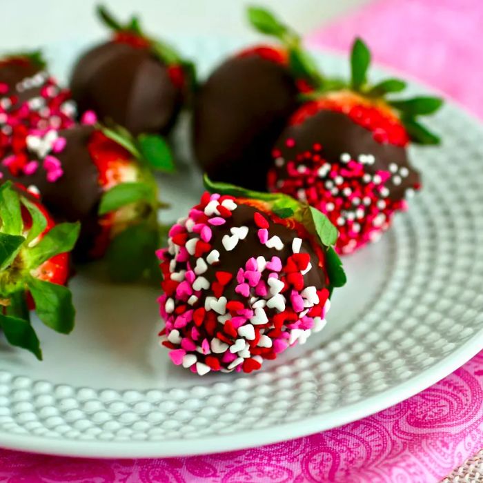 A plate of chocolate-dipped strawberries adorned with pink, red, and white mini candy heart sprinkles