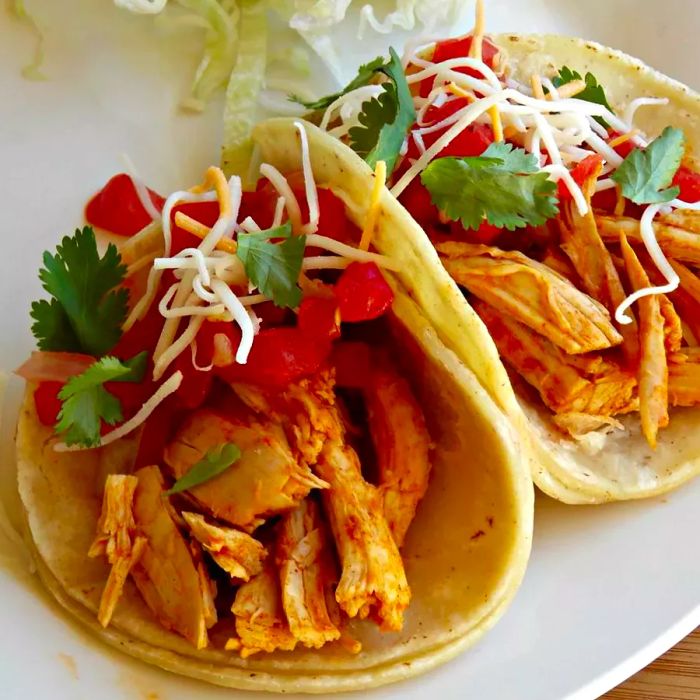 two soft chicken tacos topped with fresh garnishes on a plate