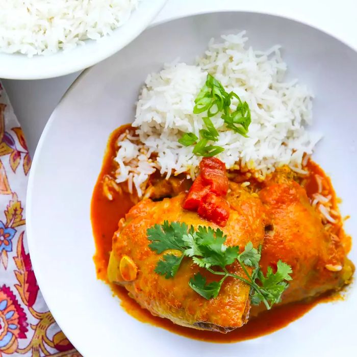 A top-down view of chicken curry served in a white bowl alongside Basmati rice, garnished with fresh cilantro.