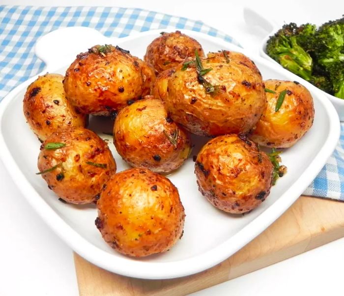 Roasted baby potatoes arranged on a white serving board with a gingham towel