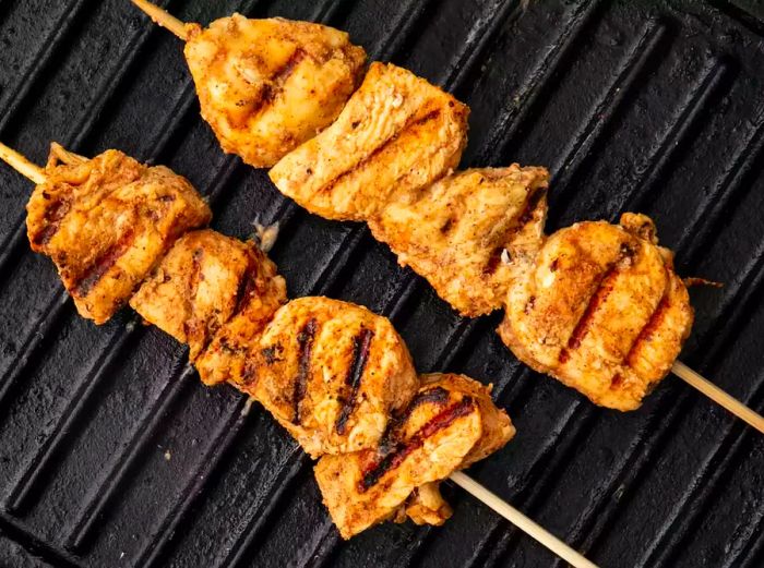 Two chicken skewers sizzling on the grill.