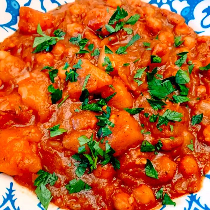 A close-up view of a bowl filled with spicy vegan potato curry, topped with fresh cilantro.