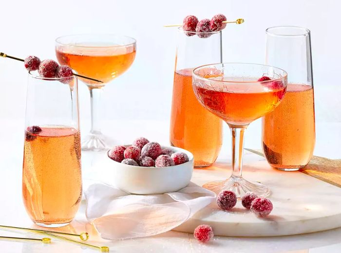 A close-up of sparkling poinsettia cocktails, garnished with fresh cranberries.