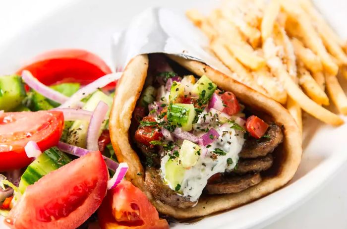 A close-up of a gyro served in a pita, accompanied by a fresh salad and crispy fries.