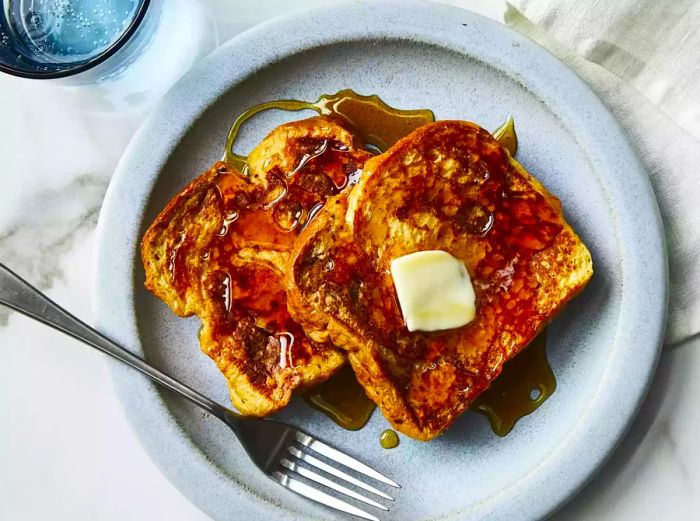 A close-up view of two perfectly golden slices of French toast, topped with melting butter and drizzled with syrup.