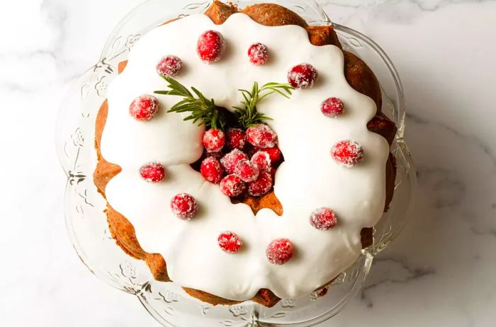 Aerial shot of a Christmas Tree Surprise Cake, topped with delicate white icing, sparkling cranberries, and sprigs of fresh rosemary.