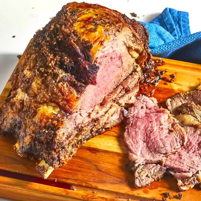 A whole prime rib resting on a cutting board with a few slices cut