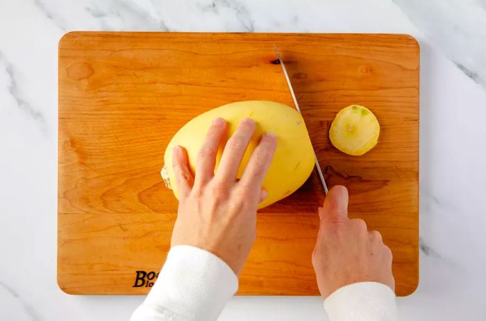 Spaghetti squash being trimmed on a cutting board