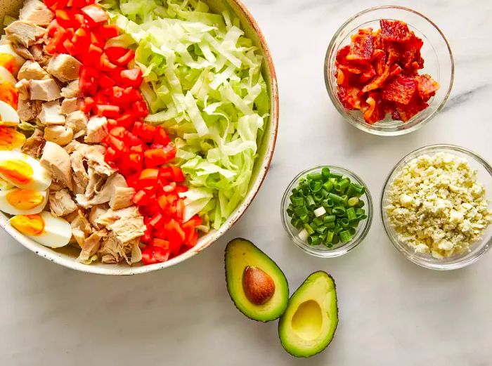 An overhead view of a Cobb salad being assembled, with fresh ingredients coming together.