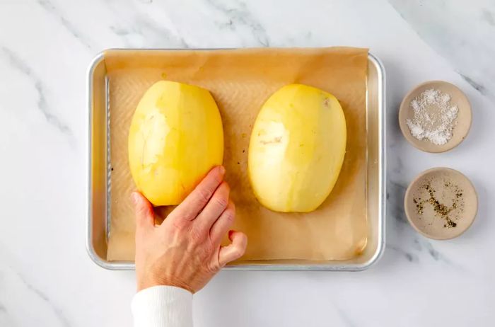 Spaghetti squash halves flipped onto a baking sheet