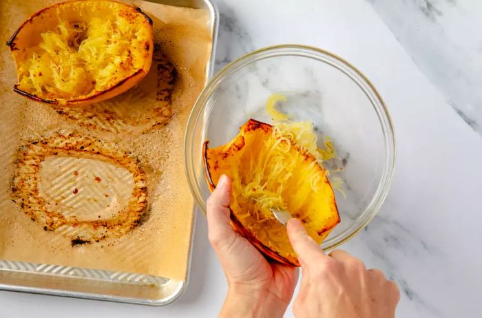 Scraping the roasted spaghetti squash strands into a bowl