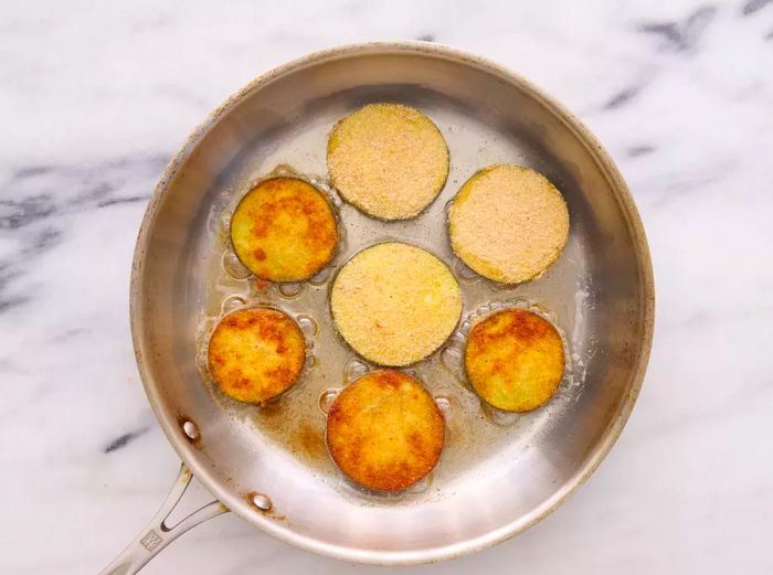 A small pan with breaded eggplant slices sizzling in hot oil.