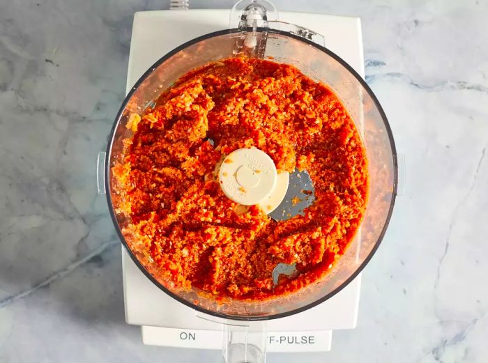 An overhead view of a food processor containing puréed vegetables for the meatloaf.