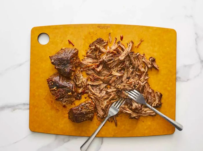 An overhead shot of barbacoa beef being shredded with two forks on a cutting board