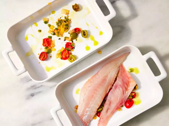 Two baking dishes: one filled with vegetables, the other with both vegetables and red snapper.