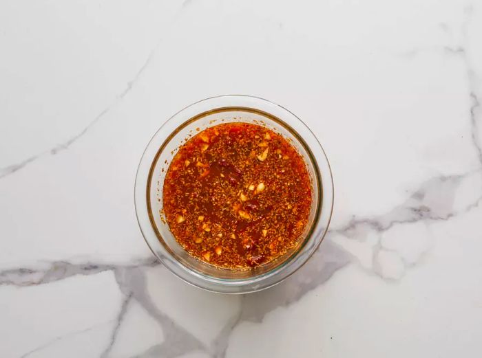 A top-down view of broth, vinegar, lime juice, chipotle peppers, garlic, cumin, oregano, and cloves mixed together in a bowl