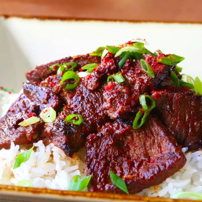 A close-up view of Bulgogi Beef served over white rice, garnished with fresh green onions in a bowl.