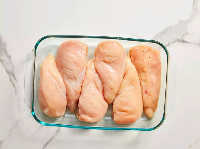 A baking dish with chicken breasts pierced with a fork all over.