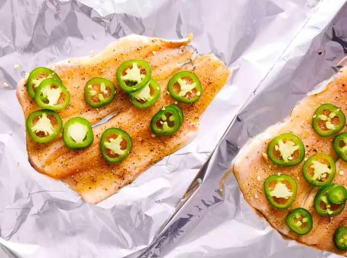 Two sheets of foil with flounder fillets topped with sliced jalapenos