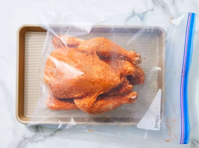 Spiced chicken inside a plastic bag resting on a baking sheet