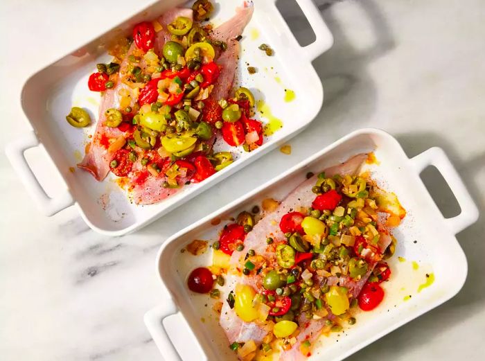 Two baking dishes, one containing vegetables and the other with both vegetables and red snapper.