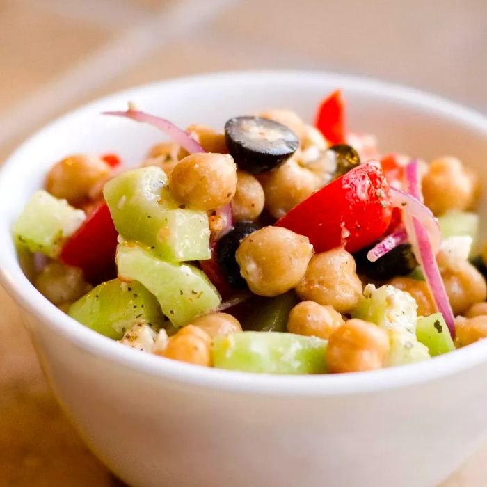 A close-up of a fresh Greek Chickpea Salad served in a white bowl.