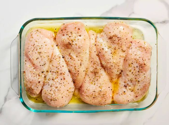 A baking dish filled with marinated chicken breasts ready for cooking.