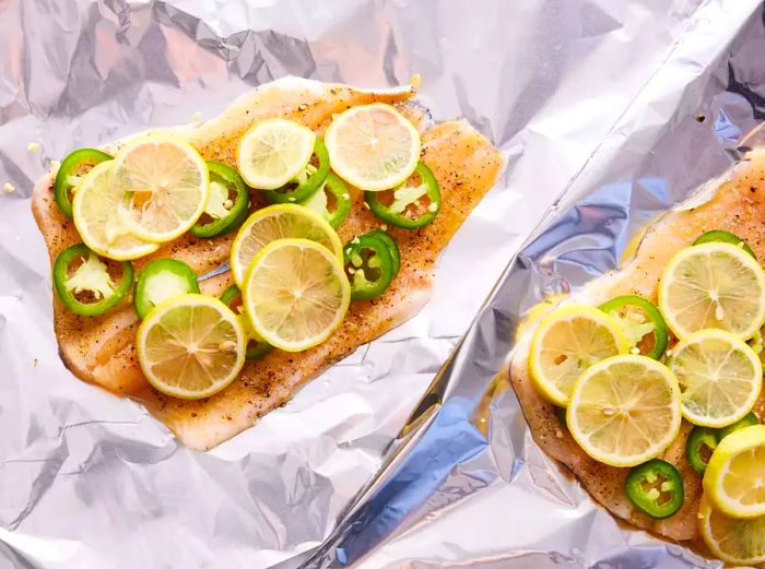 Two sheets of foil with flounder fillets, jalapeno slices, and lemon slices on top