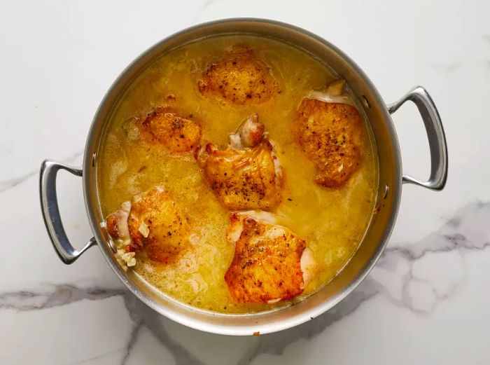 A top-down view of stock and chicken added to the pot of rice