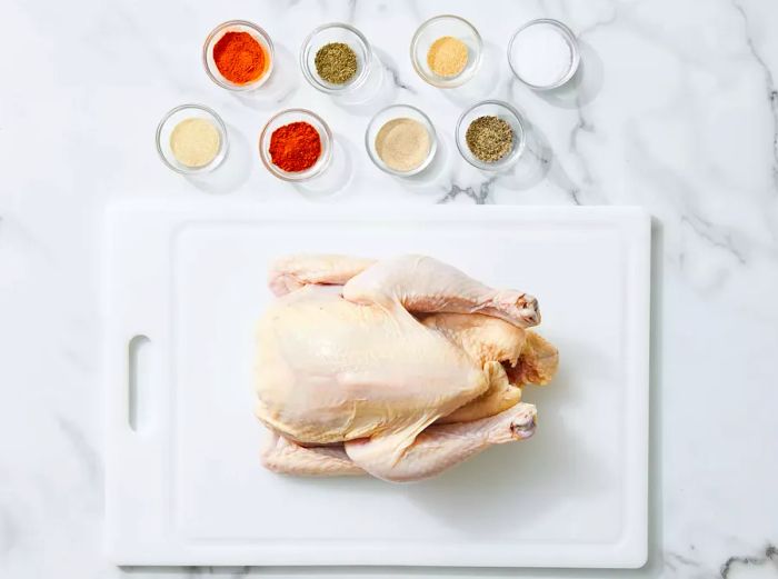 A whole chicken with ingredients arranged on a marble countertop