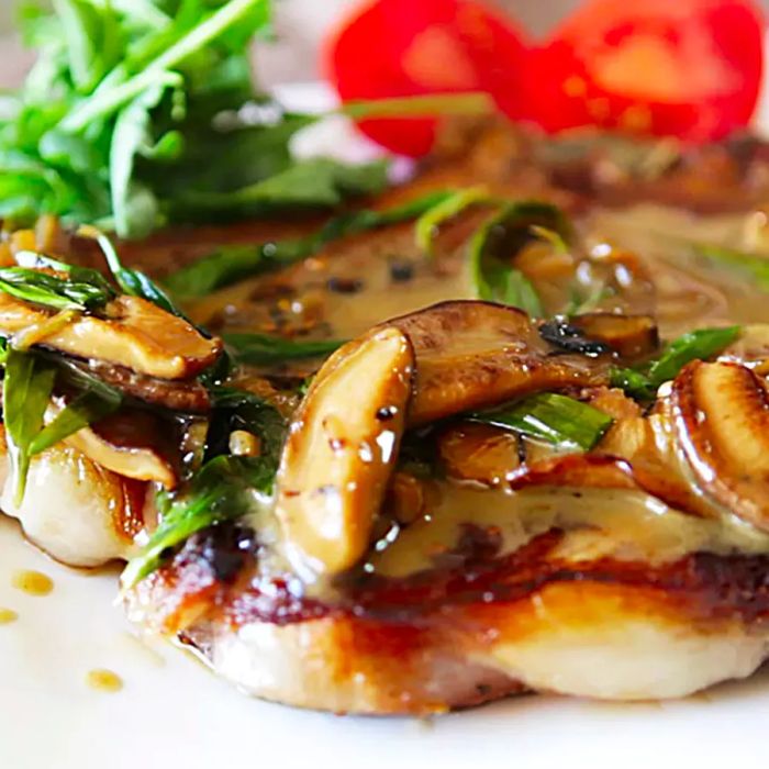 A close-up of a Sirloin Steak with Mushrooms and fresh herbs, served with a side of salad and tomatoes on a white plate.