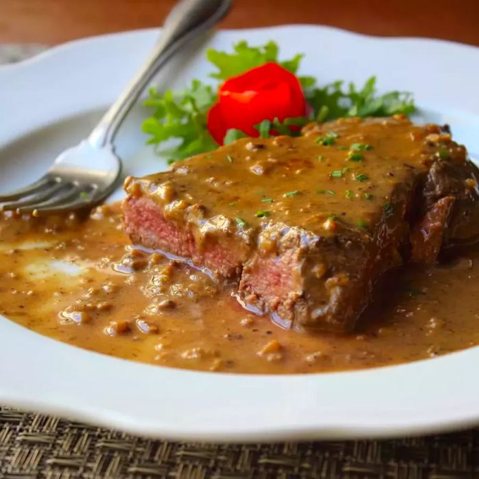 Close-up of Steak Diane with rich gravy and a fork resting on a white plate.