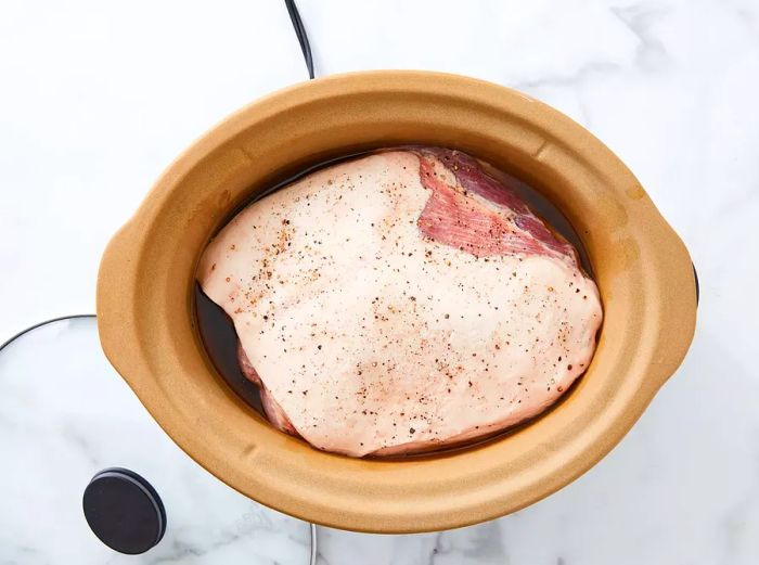 Seasoned pork shoulder placed in the slow cooker with salt and pepper.