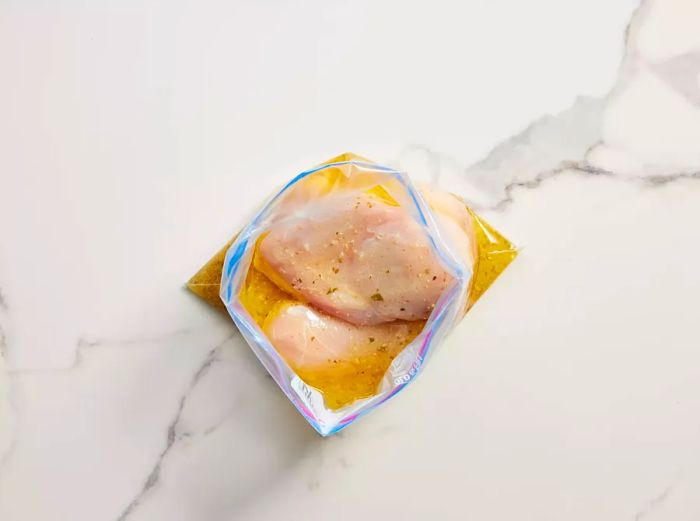 A plastic zip-top bag containing chicken breasts marinating in Italian dressing.