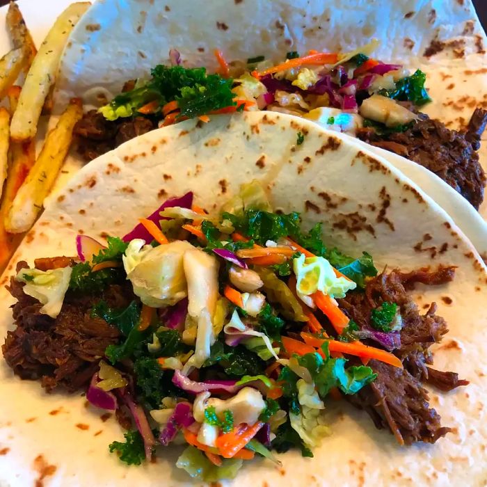 A close-up of Slow-Cooked Korean Beef Soft Tacos served alongside crispy French fries on a plate