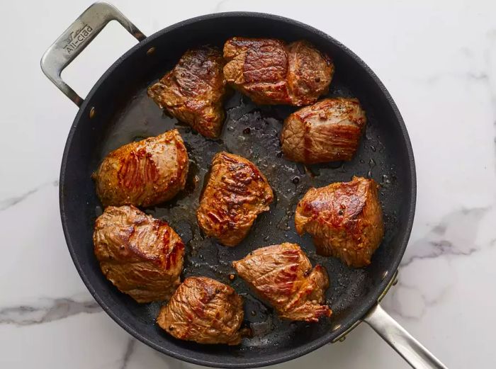 A top-down shot of beef chunks searing in a skillet