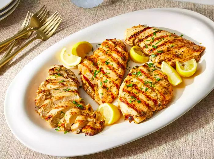 Sliced juicy grilled chicken breasts arranged with lemon wedges on a white platter