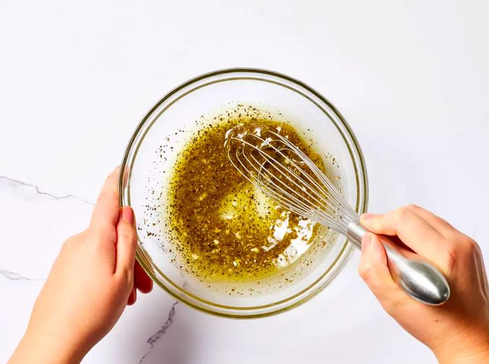 A small bowl of lemon-garlic dressing being whisked together