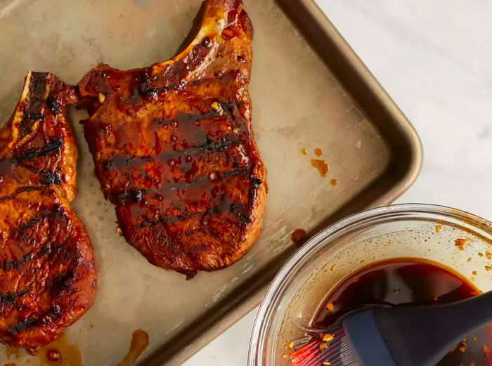 Grilled pork chops arranged on a sheet pan with the cooked marinade served on the side.