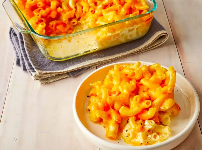 A high-angle view of a plate of baked macaroni and cheese, with more of the cheesy dish in a glass baking dish nearby.