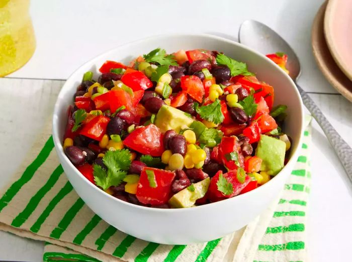 A white bowl filled with Black Bean and Corn Salad, topped with fresh herbs