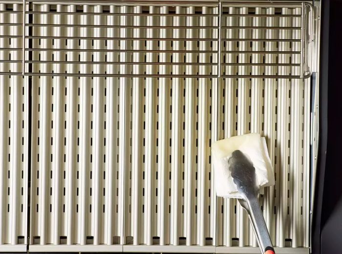 A pair of tongs holding an oiled towel, greasing the grill grates