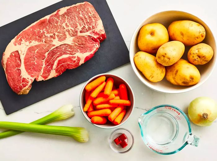 A top-down view of potatoes, onions, celery, carrots, and raw steak.